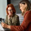 duas mulheres com roupas sociais trabalhando com o notebook em um escritório