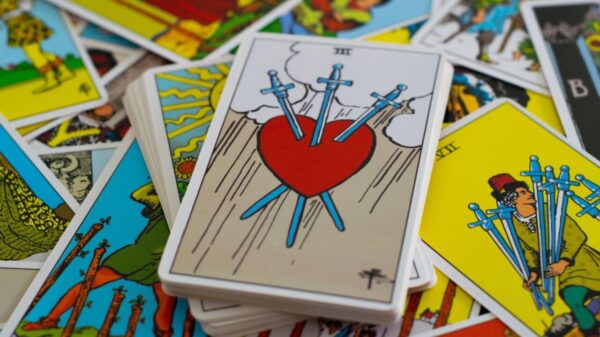 carta do tarot com um coração com espada e ao fundo outras cartas de tarot espalhadas