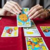 mesa de toalha vermelha com jogo de tarot e um par de mãos femininas segurando