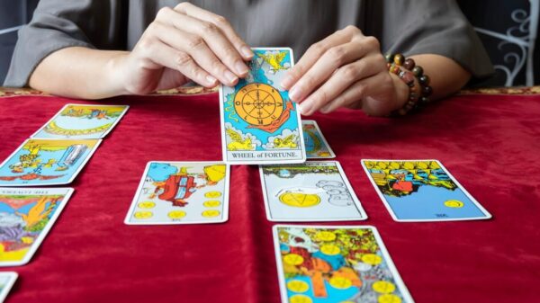 mesa de toalha vermelha com jogo de tarot e um par de mãos femininas segurando