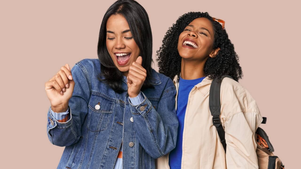 duas amigas negras sorrindo juntas em um fundo rosé
