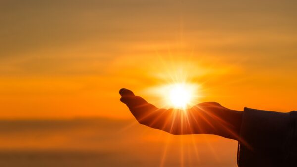 silhueta de uma mão posicionada como se estivesse segurando o sol em um céu alaranjado