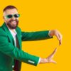 homem sorrindo com terno e óculos verde em fundo amarelo