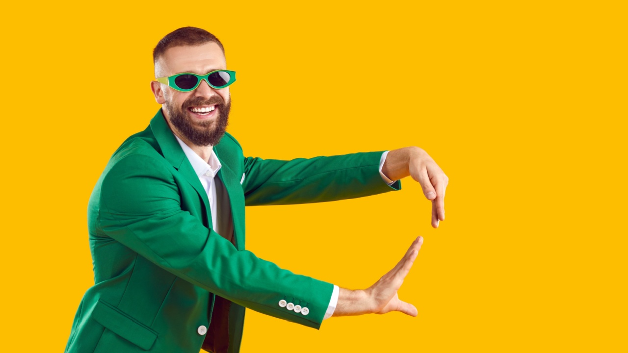 homem sorrindo com terno e óculos verde em fundo amarelo