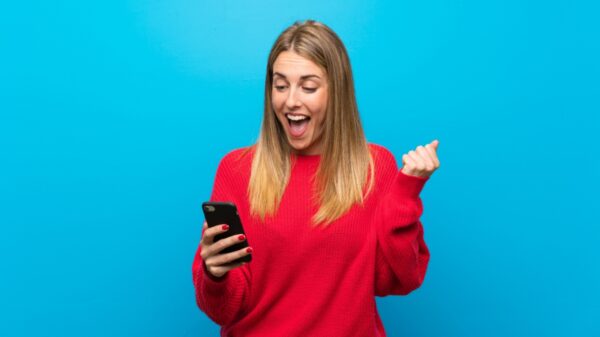 Mulher sorrindo para o celular que esta na mão direita em fundo azul