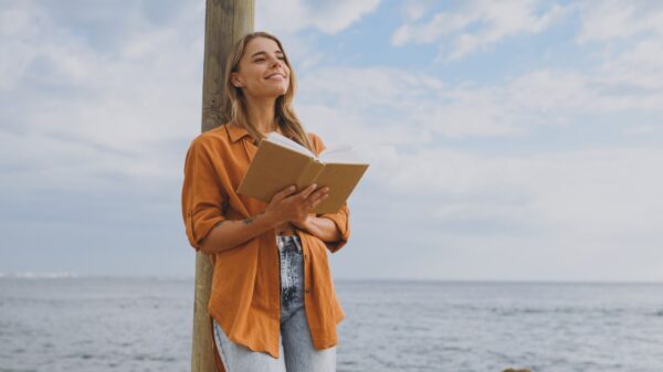 mulher encostada em um poste lendo um livro ao ar livre e próxima ao mar
