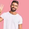 homem com camiseta branca fazendo o número quatro com os dedos em fundo rosa