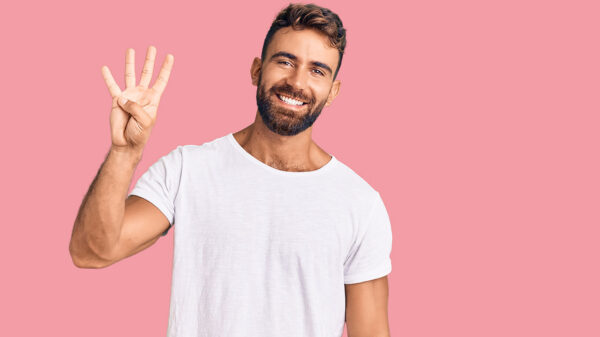 homem com camiseta branca fazendo o número quatro com os dedos em fundo rosa