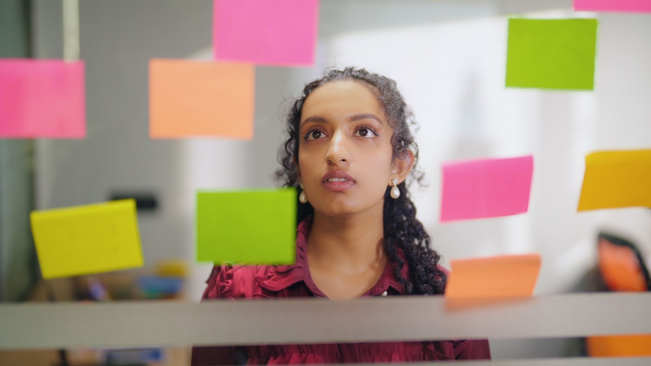 mulher negra em um escritório olhando para um vidro com post its coloridos