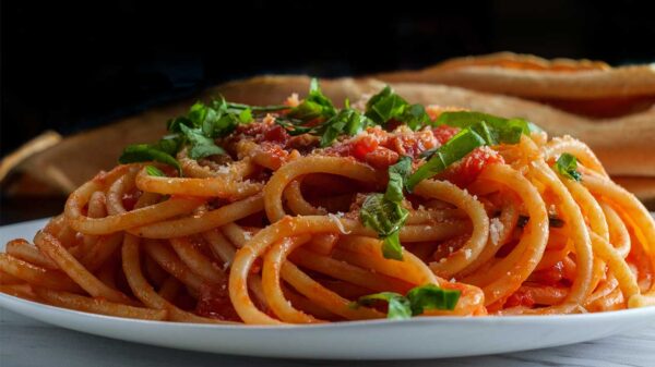 imagem de um prato branco cheio de macarrão com molho vermelho e cheiro verde