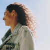 Mulher feliz e despreocupada sorrindo enquanto desfruta de um dia alegre ao ar livre com o céu azul ao fundo. Perfil lateral de uma mulher feliz sorrindo em um dia ensolarado.