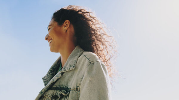 Mulher feliz e despreocupada sorrindo enquanto desfruta de um dia alegre ao ar livre com o céu azul ao fundo. Perfil lateral de uma mulher feliz sorrindo em um dia ensolarado.