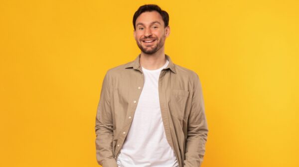 homem sorrindo com as mãos no bolso em um fundo amarelo