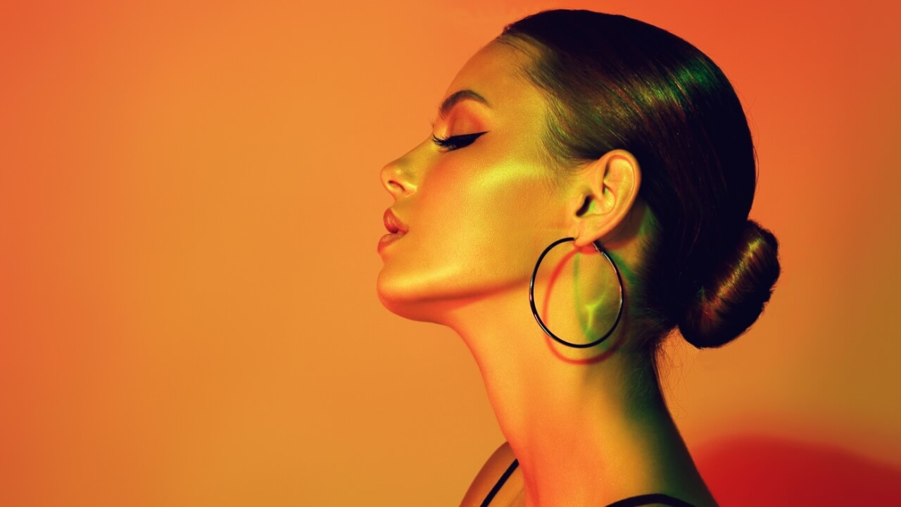 Mulher em uma luz neon e laranja com maquiagem moderna e brincos.