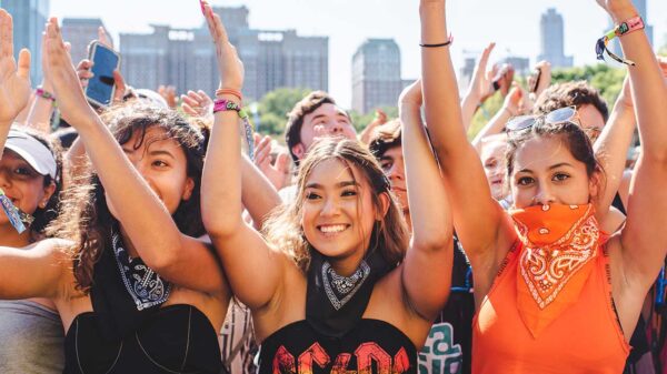 três mulheres jovens na grade do festival Lollapalooza com as mãos no alto