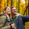casal carregando mochilas em uma paisagem de outono