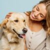 mulher jovem sorrindo e abraçando seu cachorro em fundo azul