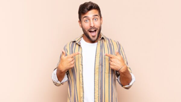 homem com a boca aberta em sorriso e apontando para si próprio em fundo rosado
