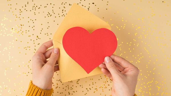 par de mãos segurando um envelope amarelo e um coração vermelho em fundo dourado