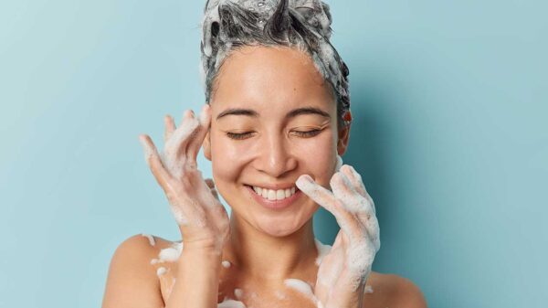 imagem do rosto de uma mulher jovem tomando banho com o cabelo ensaboado em fundo azul