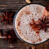 fotografia do alto de bebida com cravos da índia e canela com mais cravos da índia em cima de uma mesa de madeira