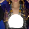 mulher com roupas ciganas olhando uma bola de cristal bastante iluminada em fundo azul e roxo