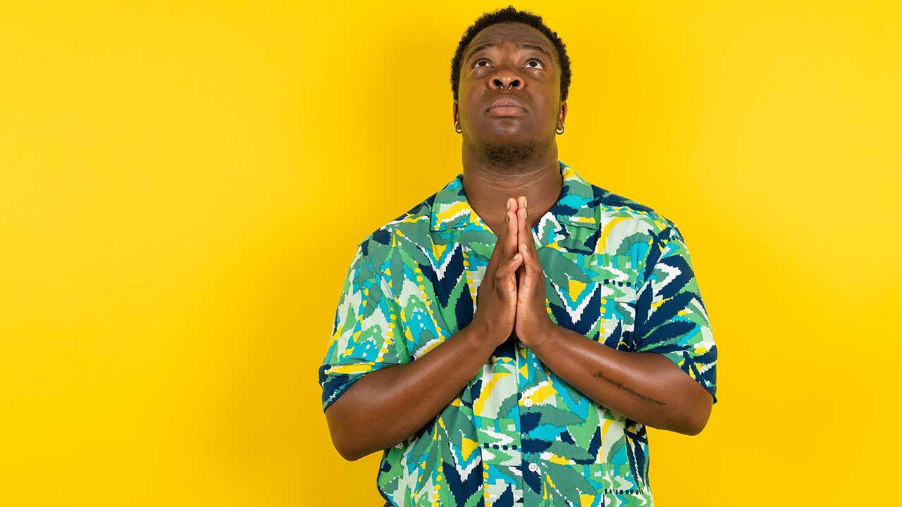 homem negro com as mãos em prece e olhando para o alto em fundo amarelo