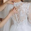 três amigas ao redor da noiva usando vestidos claros e abotoando o vestido de noiva que está ao centro