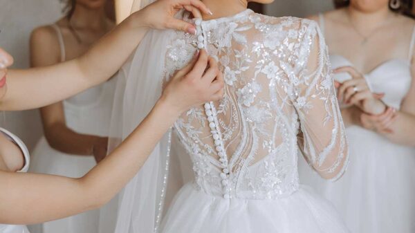 três amigas ao redor da noiva usando vestidos claros e abotoando o vestido de noiva que está ao centro
