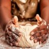 fotografia de uma mulher negra com avental sovando uma massa de pão