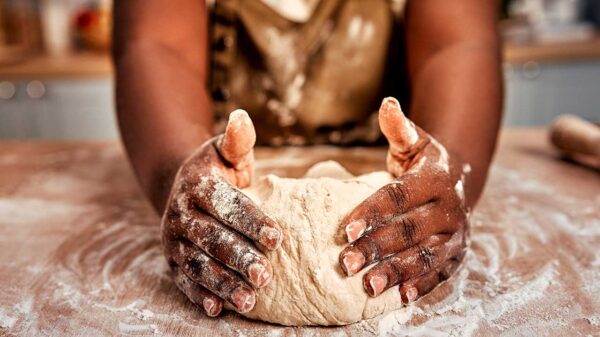 fotografia de uma mulher negra com avental sovando uma massa de pão