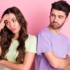 casal heterossexual de costas uma para o outro e com caras desconfiadas em fundo rosa