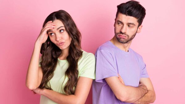 casal heterossexual de costas uma para o outro e com caras desconfiadas em fundo rosa