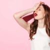 mulher jovem com expressão corporal de drama e batom vermelho em fundo rosa