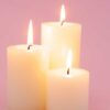 imagem de três velas brancas grossas acesas no centro de uma fundo rosa