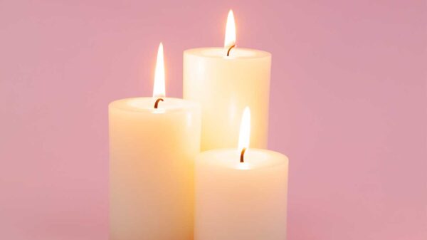 imagem de três velas brancas grossas acesas no centro de uma fundo rosa