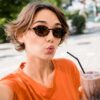 mulher usando óculos escuro tomando milk shake e fazendo biquinho para um selfie a céu aberto