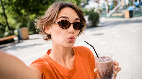 mulher usando óculos escuro tomando milk shake e fazendo biquinho para um selfie a céu aberto