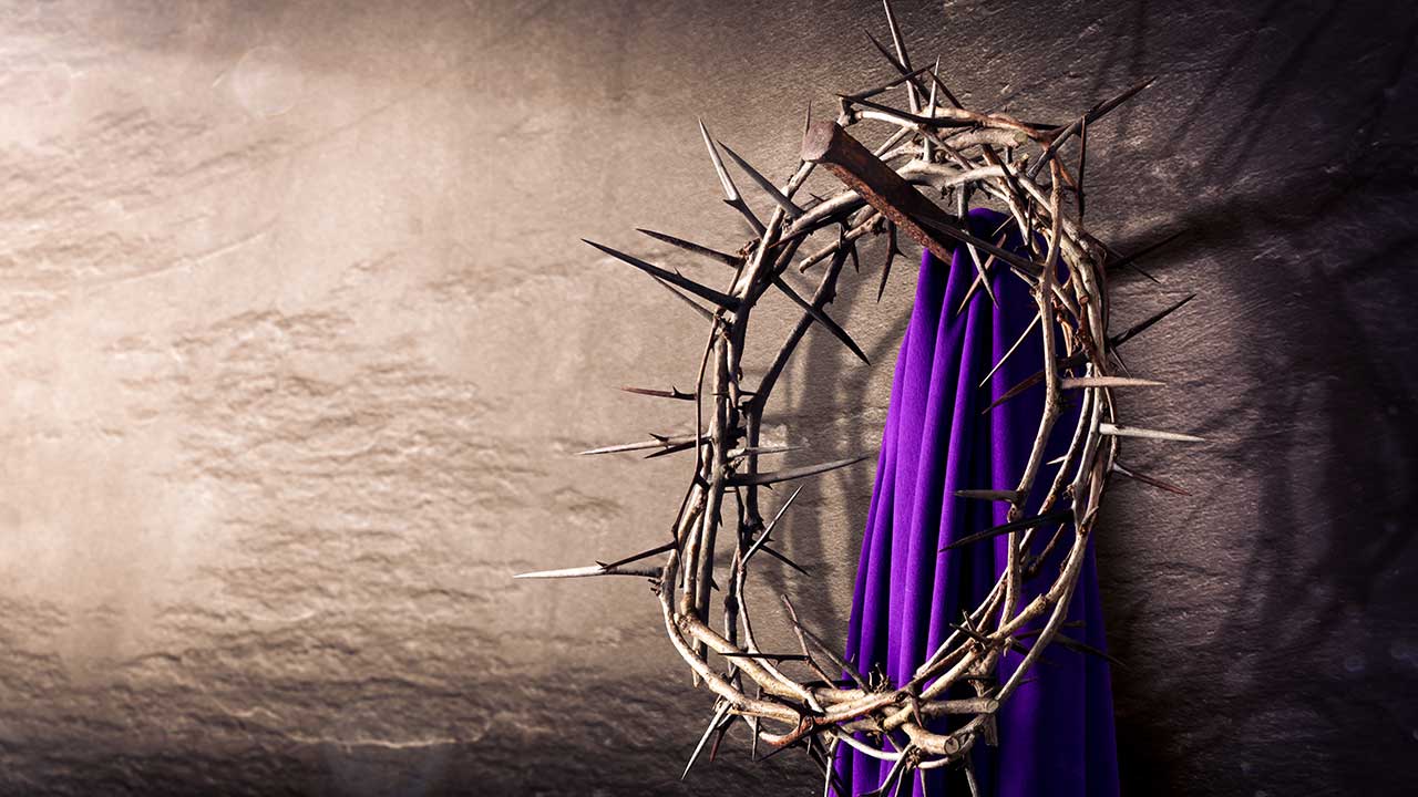imagem de uma coroa de espinhos junto a um lenço roxo em uma parede cinza