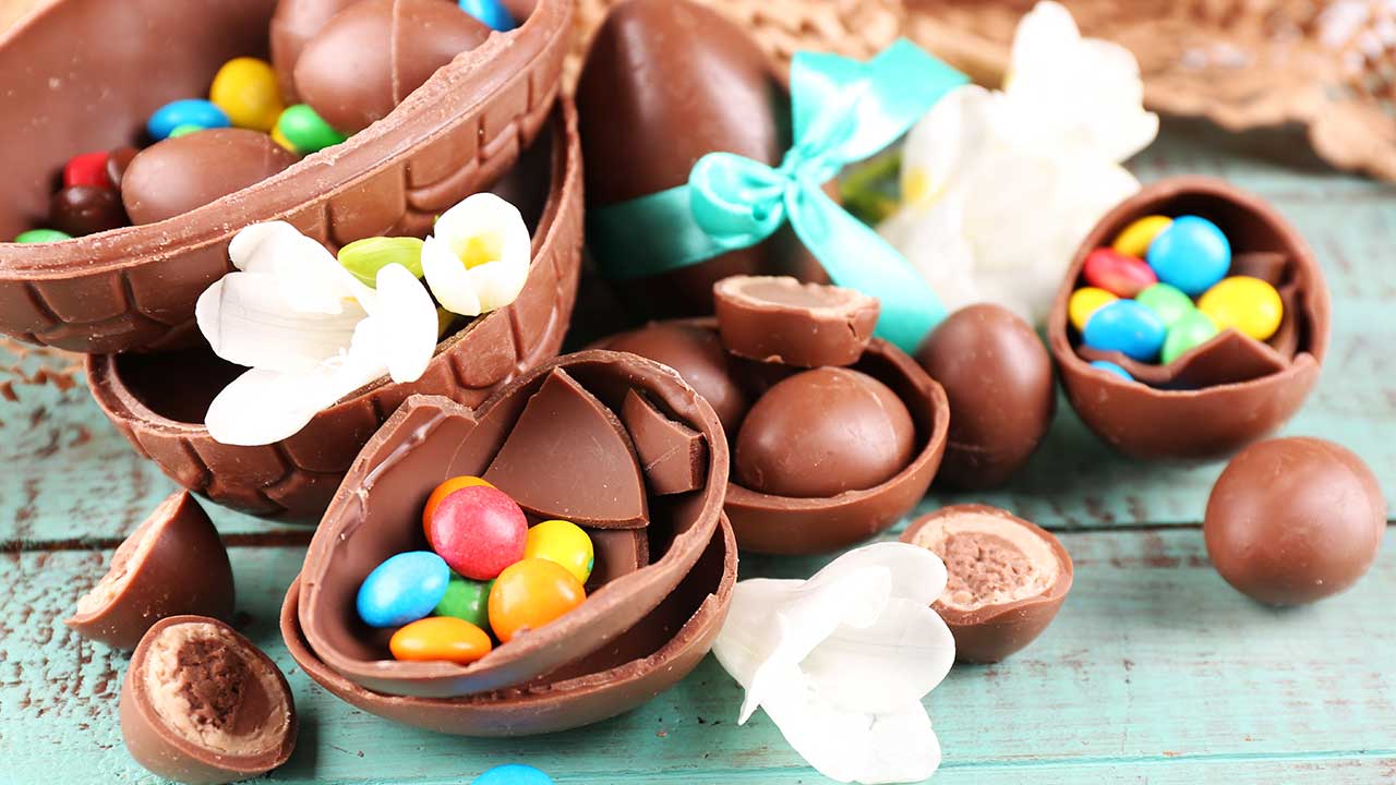 imagem com dez ovos de páscoa de chocolate em cima de uma mesa azul com três pombinhas brancas