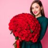 mulher jovem segurando um grande buquê de rosas vermelhas em fundo rosa