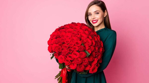 mulher jovem segurando um grande buquê de rosas vermelhas em fundo rosa