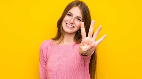 mulher jovem sorrindo fazendo o número quatro com os dedos em fundo amarelo