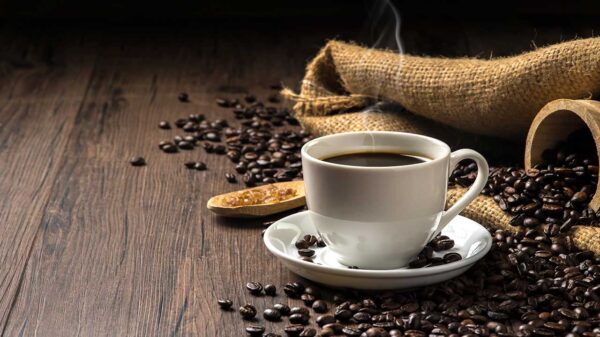 Café quente em uma xícara de café branca e muitos grãos de café colocados ao redor e açúcar em uma mesa de madeira em um ambiente quente e leve, em fundo de madeira escuro
