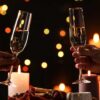 imagem de duas mãos brindando taças de champanhe e uma jantar a luz de velas