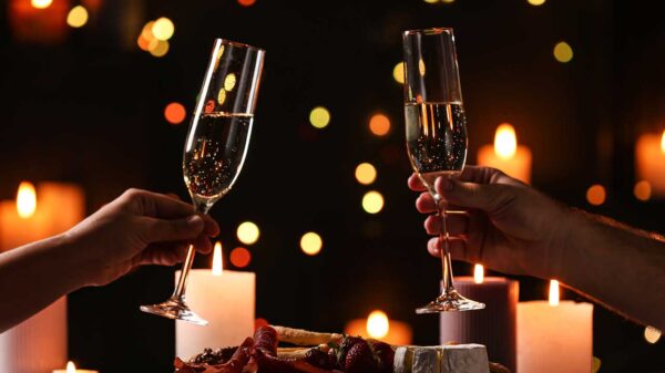imagem de duas mãos brindando taças de champanhe e uma jantar a luz de velas
