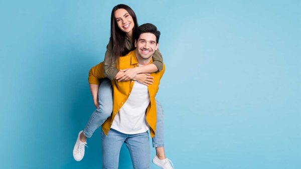 homem em pé com a namorada em suas costas os dois sorrindo em fundo azul