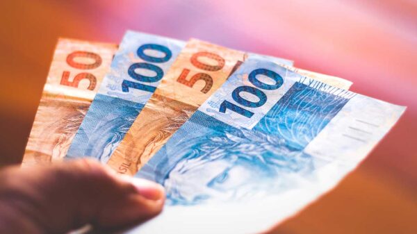 fotografia de uma mão segurando duas notas de 50 reais e duas notas de 100 reais em um fundo desfocado