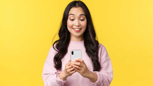 mulher olhando sorrindo para um celular que está em suas mãos em fundo amarelo