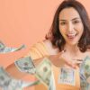 mulher jovem sorrindo de jogando notas de dollars que estava em sua mão em fundo salmão